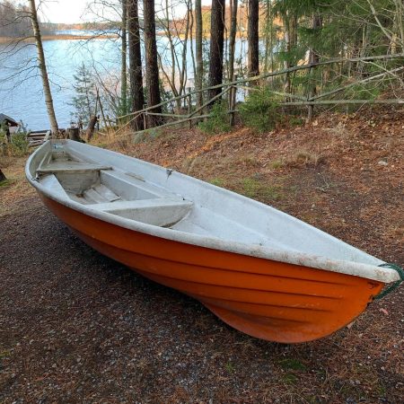 An orange and white boat sitting on the ground.